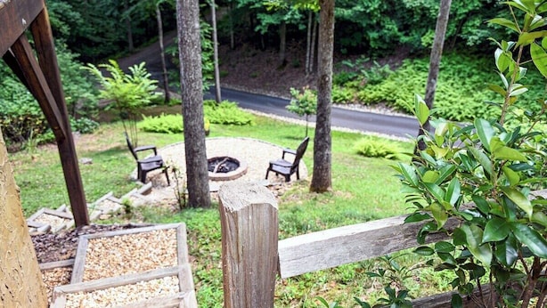 A wooden deck with a gravel area, surrounded by greenery and a fire pit.