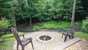A circular seating area with a fire pit, surrounded by gravel, with two Adirondack chairs and a wooden bench.