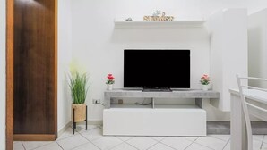 Una sala de estar moderna con un televisor de pantalla plana montado en una consola blanca, una puerta de madera a la izquierda y una silla blanca a la derecha.