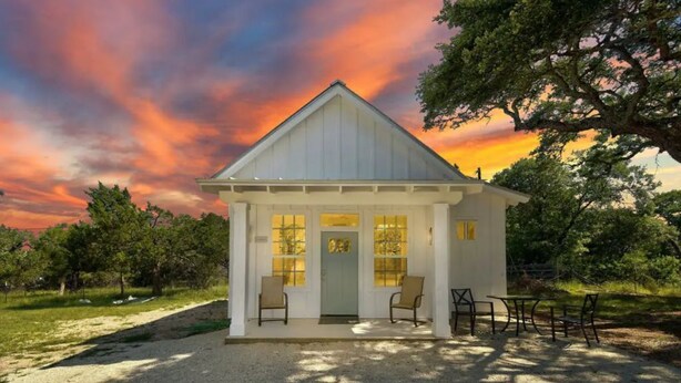A small white building with a gabled roof, a front door, and two chairs outside. - Romantic Bungalow "Carmen" on 30 Acres (Dripping Springs)