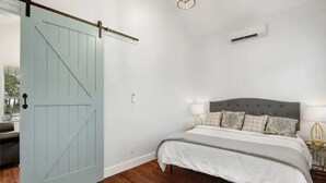 A bedroom with a bed, bedside lamps, a wall-mounted air conditioner, and a sliding door. - Romantic Bungalow "Carmen" on 30 Acres (Dripping Springs)