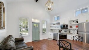 A modern kitchen with white cabinets, stainless steel appliances, and a dining area with a wooden table and chairs. - Romantic Bungalow "Carmen" on 30 Acres (Dripping Springs)