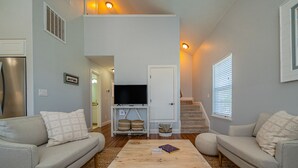 Ein Wohnzimmer mit zwei Sofas, einem Couchtisch, einem Fernseher auf einem Schrank und einer Treppe, die zu einer oberen Ebene führt.