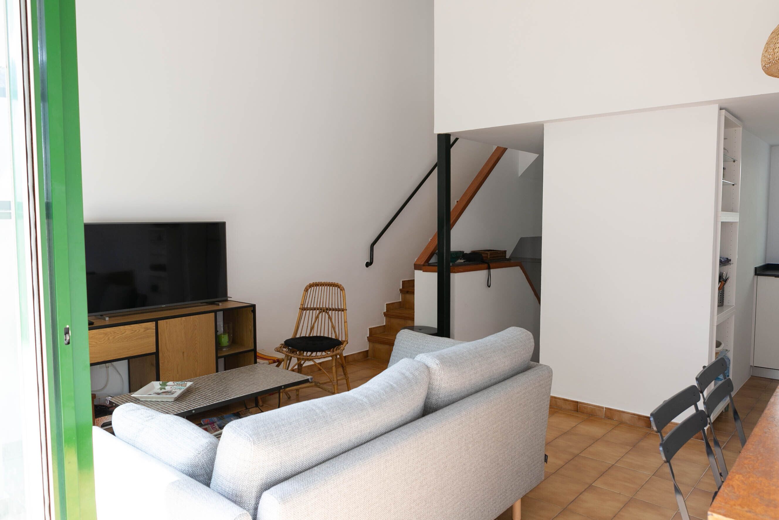 A living room with a sofa, a television, a dining table, and a staircase leading to an upper level.