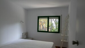 Une chambre à coucher avec un lit, une fenêtre, un mur blanc et un plancher en bois.
