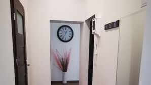 A hallway with a wooden floor, a red mat, a clock, and a white wall with a plant. - Apartament Ogarna II (Gdansk)