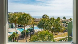 A view of a pool area with palm trees, a clear sky, and the ocean in the background. - Newly Remodeled Bathrooms - 8D Mariners Walk - Ocean Views - Wild Dunes (Isle Of Palms)