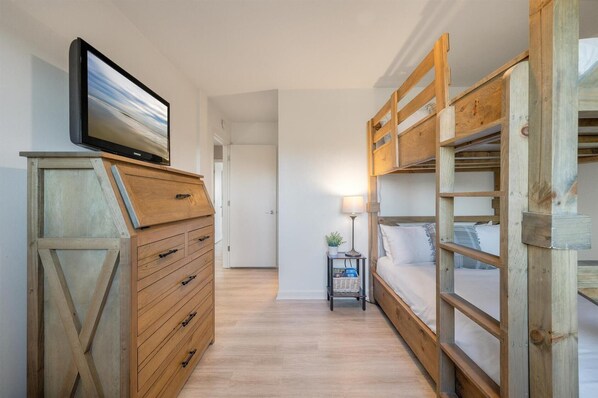 A narrow hallway with wooden bunk beds on one side and a wooden dresser with a television on the other. - Newly Remodeled Bathrooms - 8D Mariners Walk - Ocean Views - Wild Dunes (Isle Of Palms)