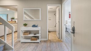 A hallway with a white console table, a mirror, and a door leading to a bathroom. - Newly Remodeled Bathrooms - 8D Mariners Walk - Ocean Views - Wild Dunes (Isle Of Palms)