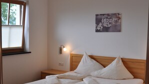 Een net opgemaakt bed met witte lakens, een houten hoofdbord en een nachtkastje met een lamp.