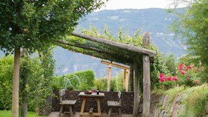 Een rustieke buitenruimte met een houten pergola, een stenen muur en een tafel gedekt met wijnglazen en flessen.