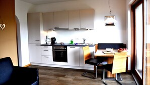 Een kleine keuken met witte kastjes, een ingebouwde oven en een eethoek met een houten tafel en stoelen.