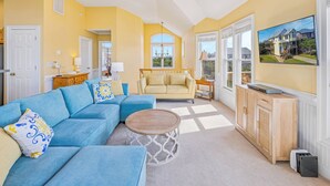 A living room with a blue sectional sofa, a round coffee table, and a television on a wooden cabinet. - Oceanside Dog Friendly Home w/ Hot Tub, Game Room, and Wet Bar. Island Stylin'! (Frisco)