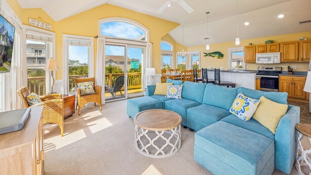 A spacious living room with a blue sectional sofa, a round coffee table, and wicker chairs. - Oceanside Dog Friendly Home w/ Hot Tub, Game Room, and Wet Bar. Island Stylin'! (Frisco)