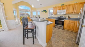 A kitchen with wooden cabinets, a central island, a stove, and a microwave. - Oceanside Dog Friendly Home w/ Hot Tub, Game Room, and Wet Bar. Island Stylin'! (Frisco)