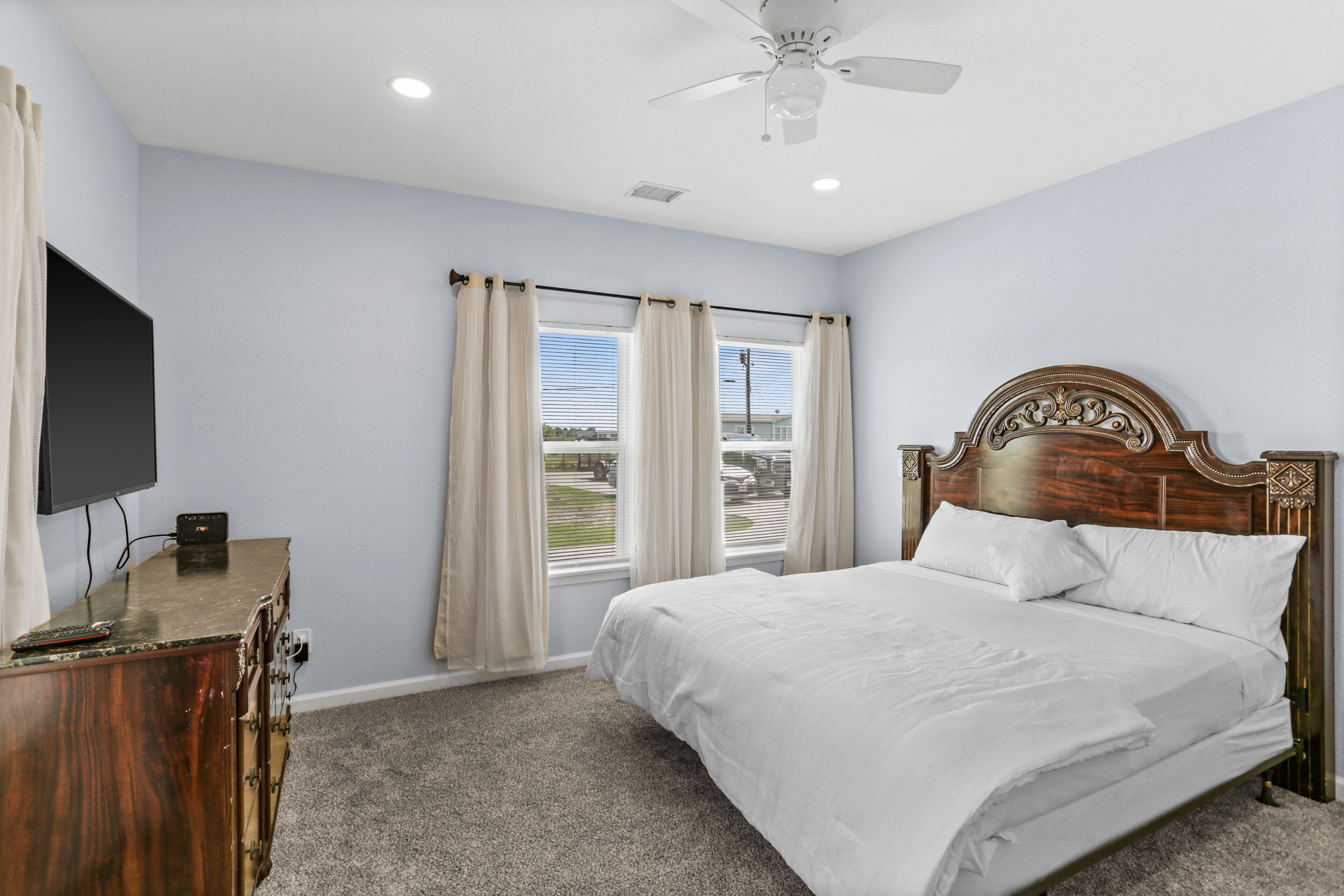 A bedroom with a bed, a television on a dresser, and windows with curtains.
