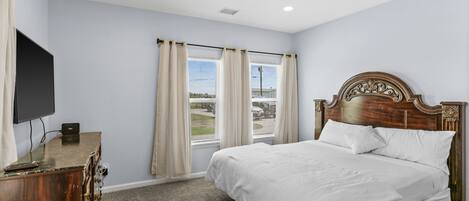 A bedroom with a bed, a television on a dresser, and windows with curtains.