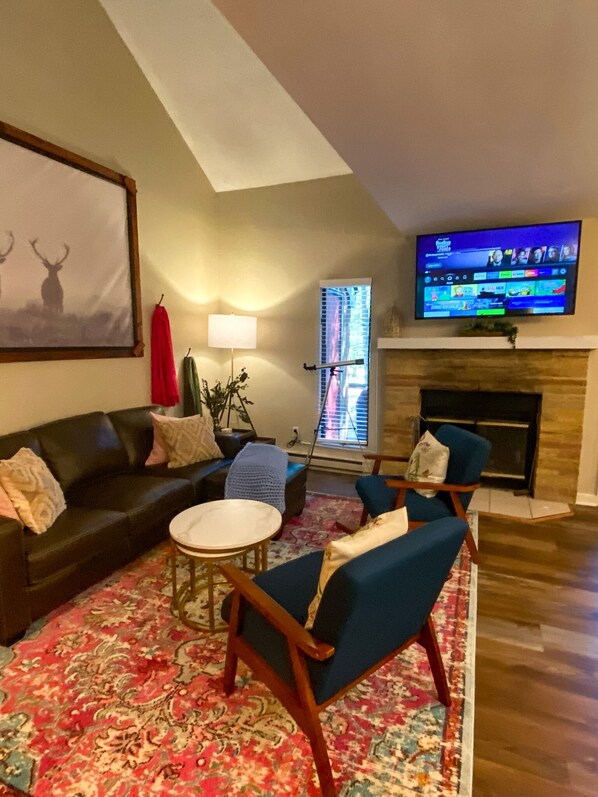 Un salon avec une cheminée, un téléviseur fixé au mur, un canapé, deux fauteuils, une table basse et un grand tableau représentant des cerfs.