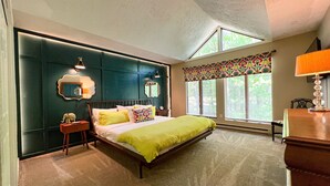 Ein Schlafzimmer mit einem Bett, Nachttischen, einem Spiegel und einem Fenster mit Jalousien.