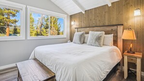 A bedroom with a wooden headboard, a large bed with white bedding, a bench, and a nightstand with a lamp.
