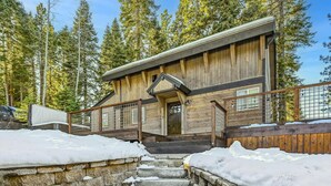 A wooden cabin with a stone staircase leading to a wooden deck, surrounded by trees and covered in snow.