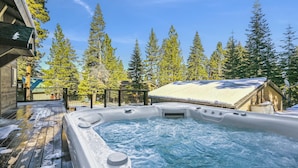 A hot tub surrounded by snow-covered trees and a wooden deck.