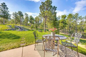 An outdoor patio with a round table and chairs, surrounded by a grassy area with trees and a stone arrangement. - Hot Tub! Mtn-View Family Haven in Black Forest (Colorado Springs)