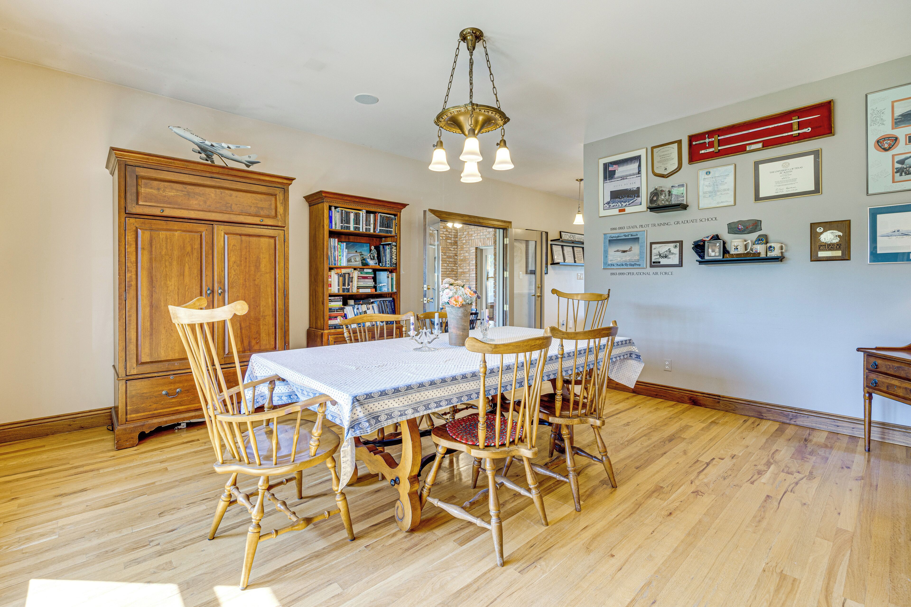 A dining room with a wooden table and chairs, a chandelier, and a bookshelf.