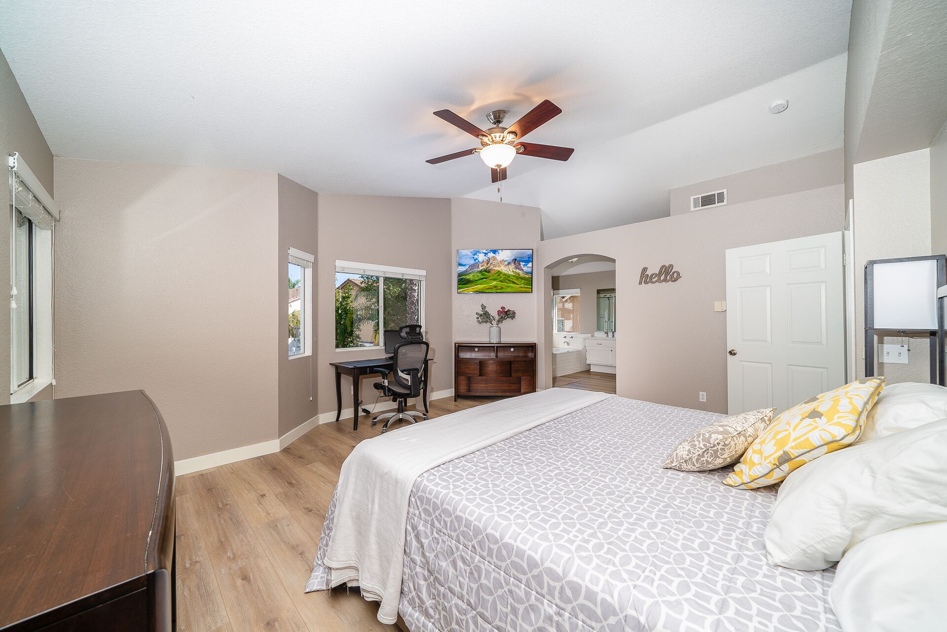 A bedroom with a bed, a desk, a chair, a ceiling fan, and a window.
