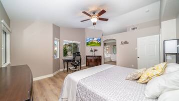 A bedroom with a bed, a desk, a chair, a ceiling fan, and a window.