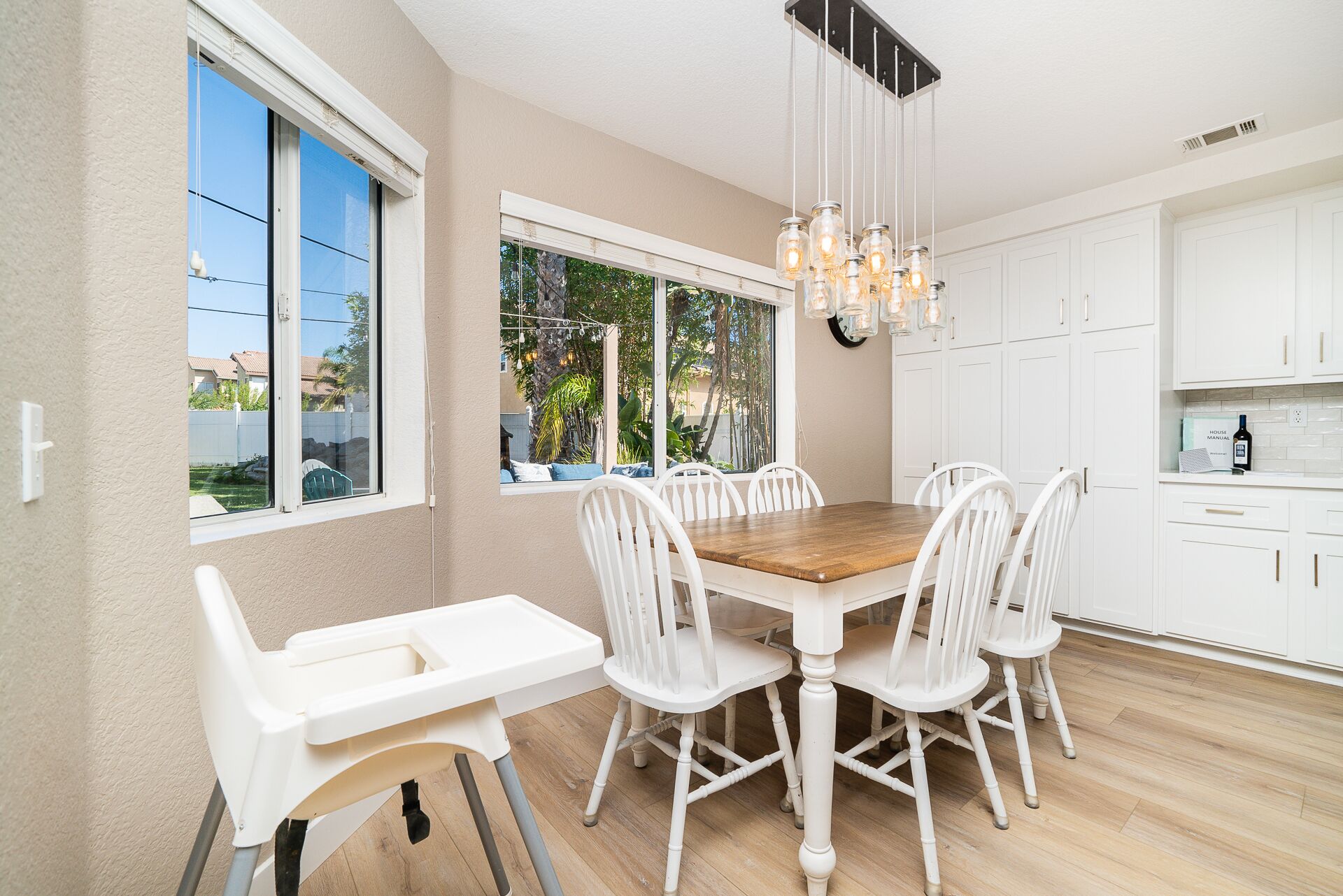 A modern kitchen with white cabinetry, a wooden dining table, and a hanging light fixture.