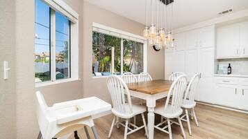 A modern kitchen with white cabinetry, a wooden dining table, and a hanging light fixture.