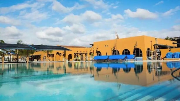 En swimmingpool med et spejlbillede af en bygning med buede vinduer og et blåt tag.