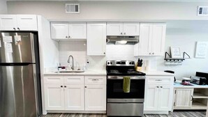 Una cocina moderna con gabinetes blancos, electrodomésticos de acero inoxidable y piso estampado.