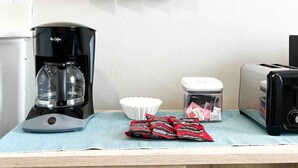 Una cocina con cafetera, tostadora, un tazón y una estantería con tazas.