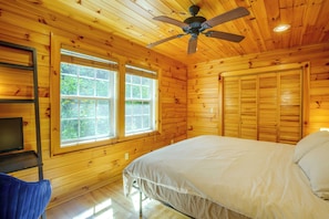 Ein Schlafzimmer einer Holzhütte mit einem Bett, einem Schreibtisch und einem Deckenventilator.