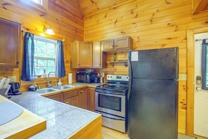 A compact kitchen with wooden walls, a stainless steel refrigerator, a microwave, an oven, and a sink. - Cozy Boone Cabin w/ Deck: Close to Downtown! (Boone)