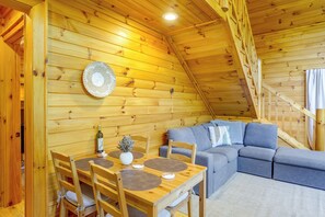 Ein gemütliches Holzinnere mit Esstisch, Stühlen, einer Couch und einer Treppe.