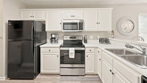 A modern kitchen with white cabinetry, a black refrigerator, a microwave, an oven, a coffee maker, and a toaster. - TB 22A Edge of Seventeen Beautiful 3 bedroom True Blue condo (Pawleys Island)