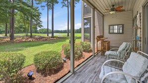 A covered porch with a view of a golf course, a seating area with chairs, and a small table. - TB 22A Edge of Seventeen Beautiful 3 bedroom True Blue condo (Pawleys Island)