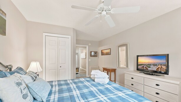 A bedroom with a bed, a television, a ceiling fan, and a door leading to another room. - TB 22A Edge of Seventeen Beautiful 3 bedroom True Blue condo (Pawleys Island)