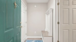 A hallway with a teal door, a white door, and a light-colored wall. There is a small shelf with hooks and a white ceiling light. - TB 22A Edge of Seventeen Beautiful 3 bedroom True Blue condo (Pawleys Island)