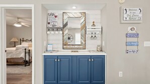 A bathroom with a blue vanity, a mirror with a decorative frame, and various wall-mounted items including a clock and a sign. - TB 22A Edge of Seventeen Beautiful 3 bedroom True Blue condo (Pawleys Island)