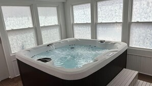 Ein Whirlpool in einem Raum mit großen Fenstern, Holzboden und einer Bank.