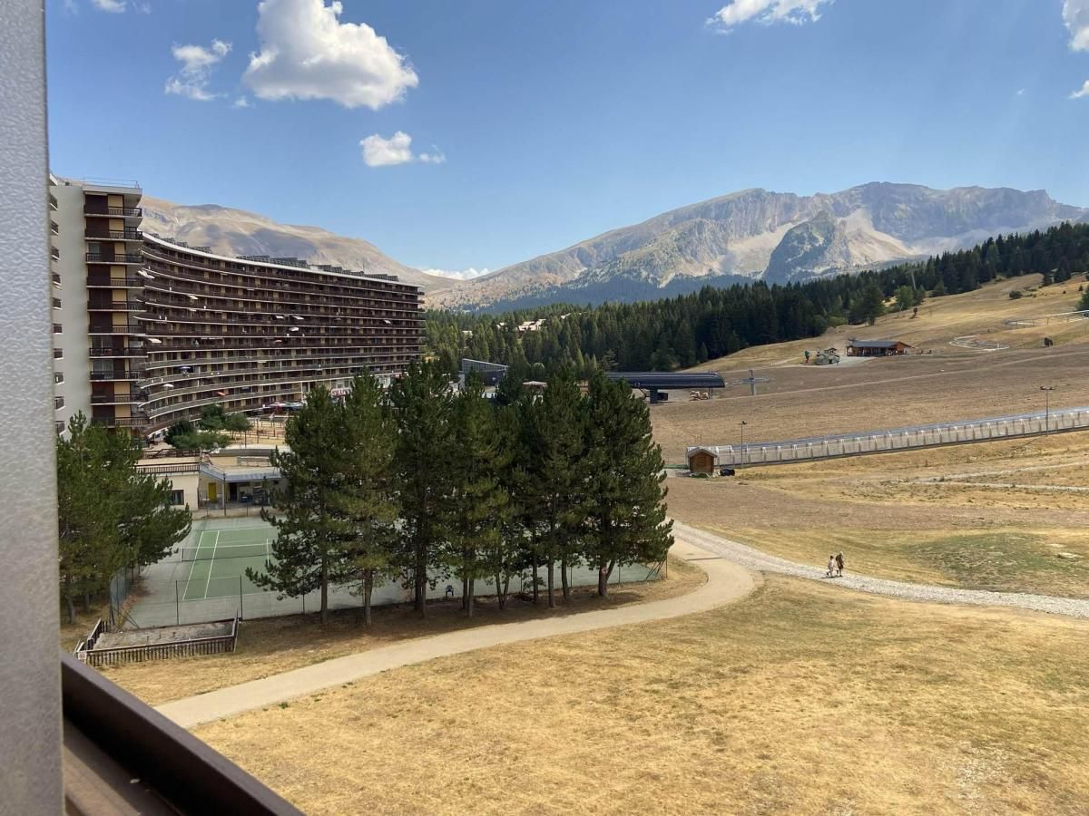 A hotel with a curved facade, a tennis court, and a mountainous backdrop.