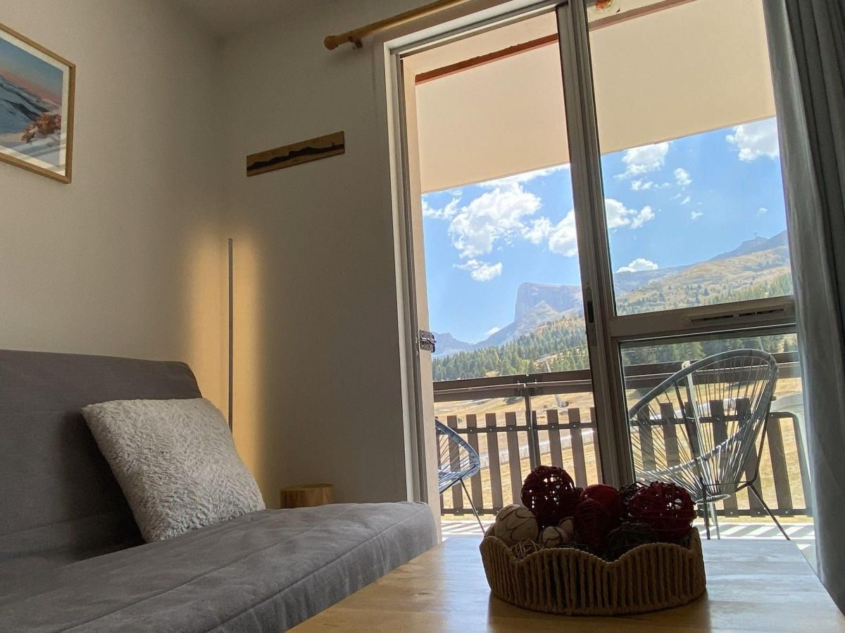 A room with a sofa, a window with a view of mountains, and a basket of fruit on a table.