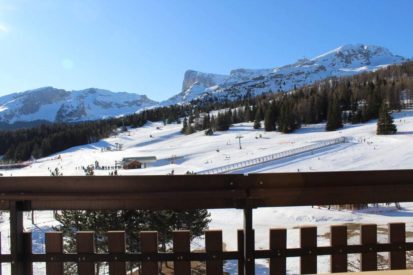 Ein mit Schnee bedeckter Skipisten mit einem Holzzaun im Vordergrund.