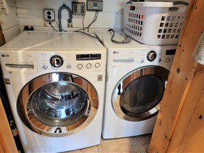 Two white LG front-loading washing machines with control panels, a white laundry basket, and a white dryer.