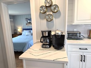 A compact kitchenette with a coffee maker, toaster, and wall-mounted clocks.