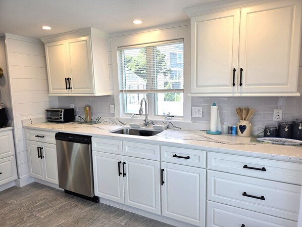 A modern kitchen with white cabinetry, stainless steel appliances, and a window with blinds.